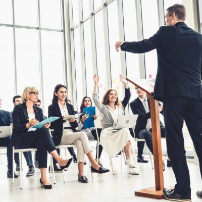 Group of business people meeting in a seminar conference . Audience listening to instructor in employee education training session . Office worker community summit forum with expert speaker .